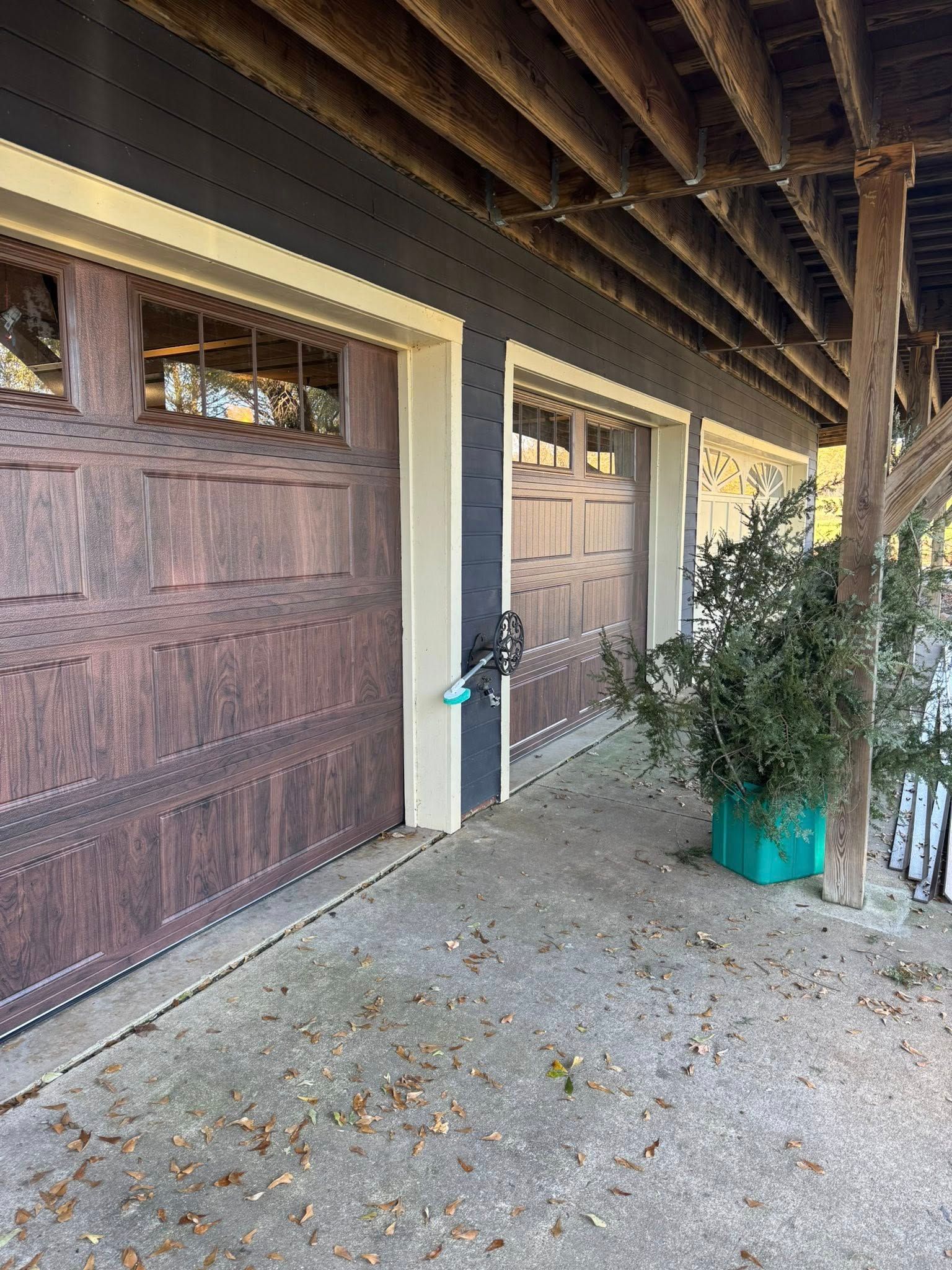 Rustic porch with two garage-style doors, a potted plant, and gravel ground under a wooden roof.