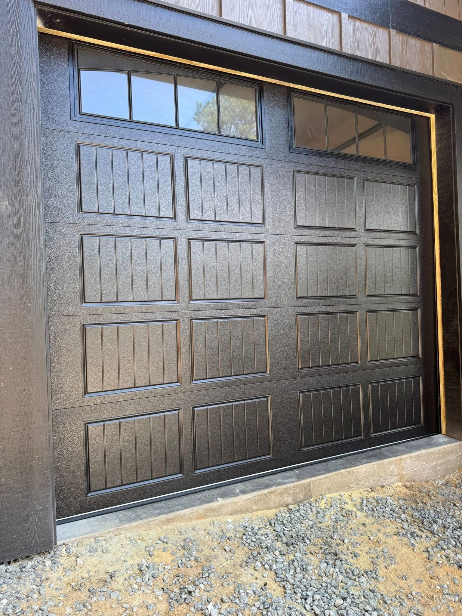 Black paneled garage door with frosted windows above, set in a dark exterior wall.