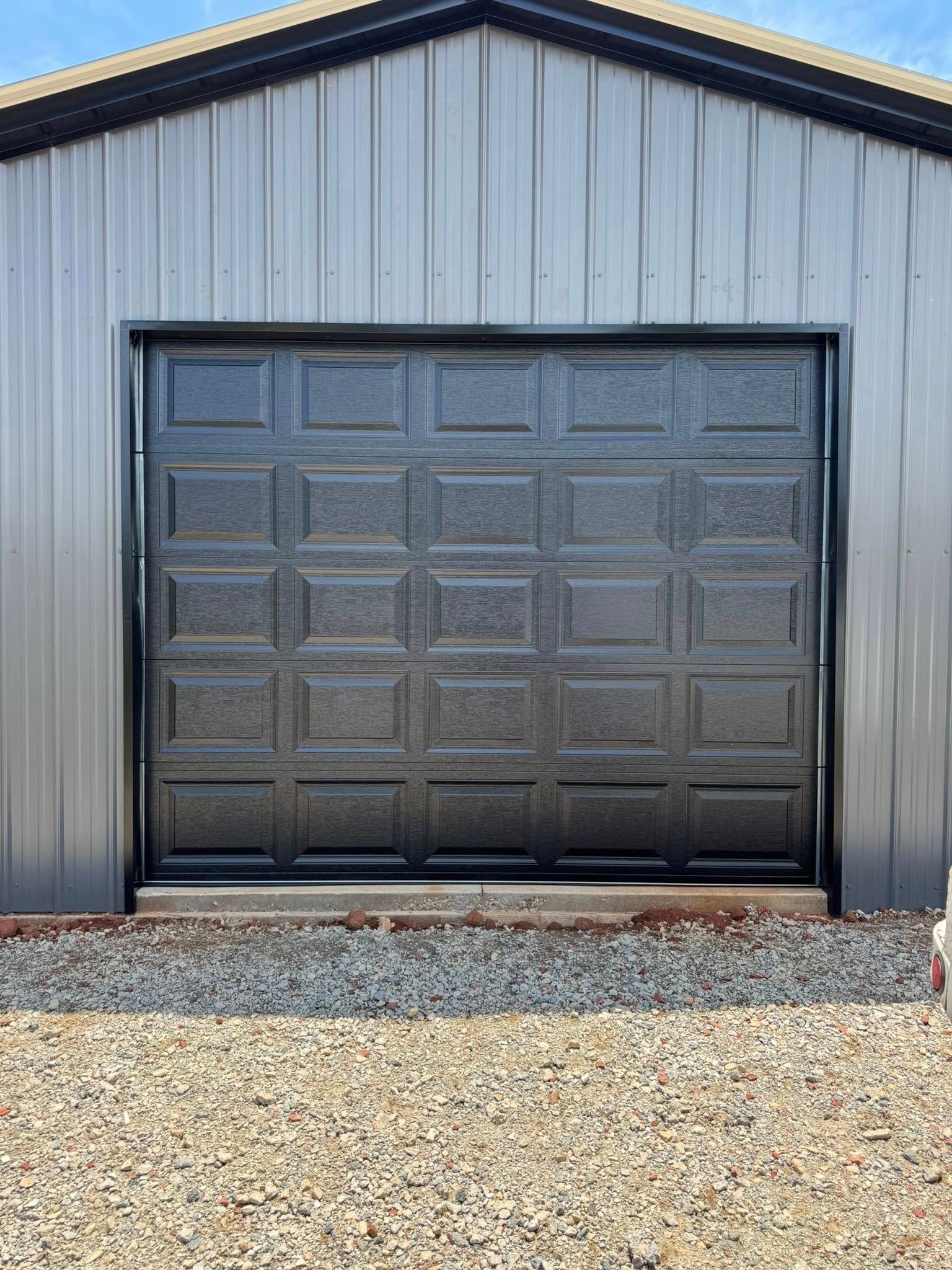 Black garage door on a gray metal building with a gravel foreground