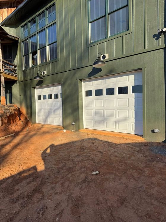 Green house exterior with two white garage doors and a dirt driveway in front