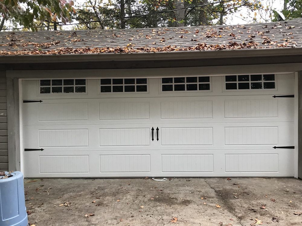 White two-car garage door with small windows under a roof covered in leaves.