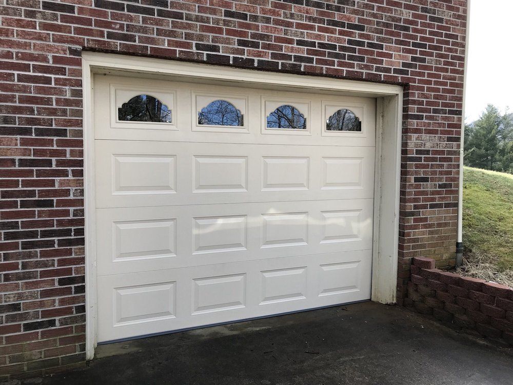 White garage door with four small arched windows set in a brick house exterior.
