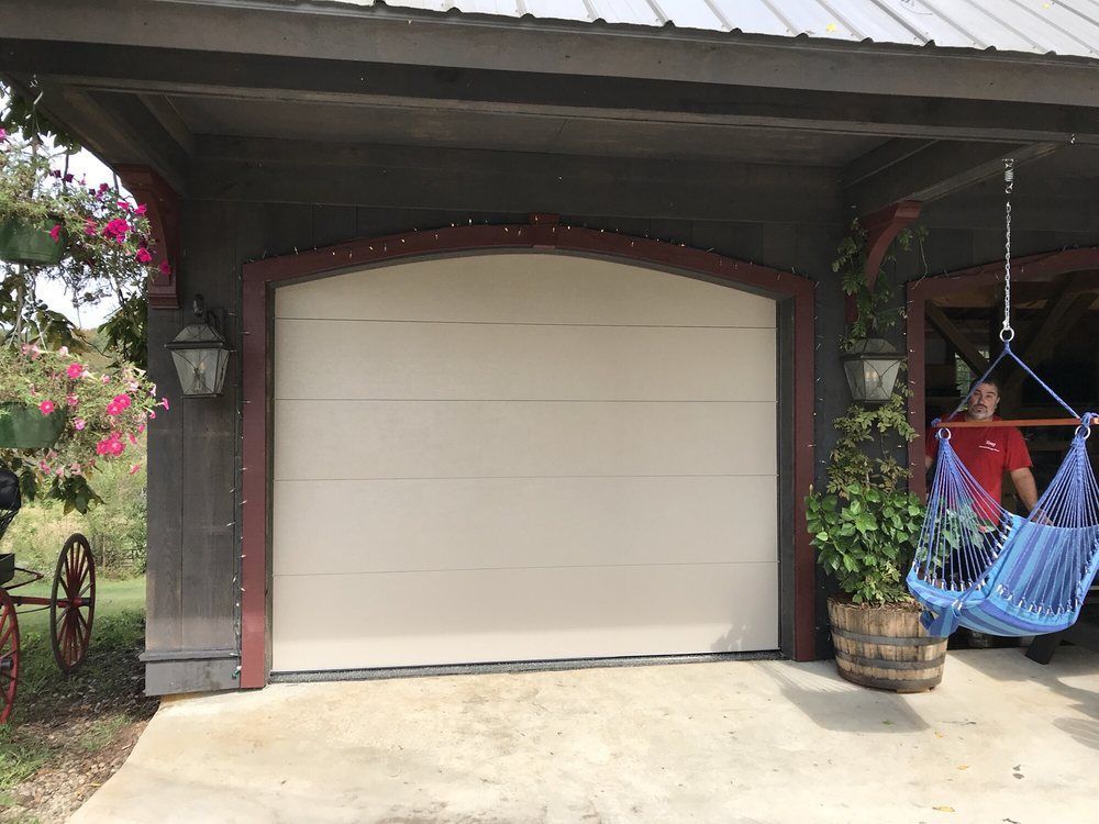 Garage door beneath a porch, with a hanging blue chair and potted plants on the right.