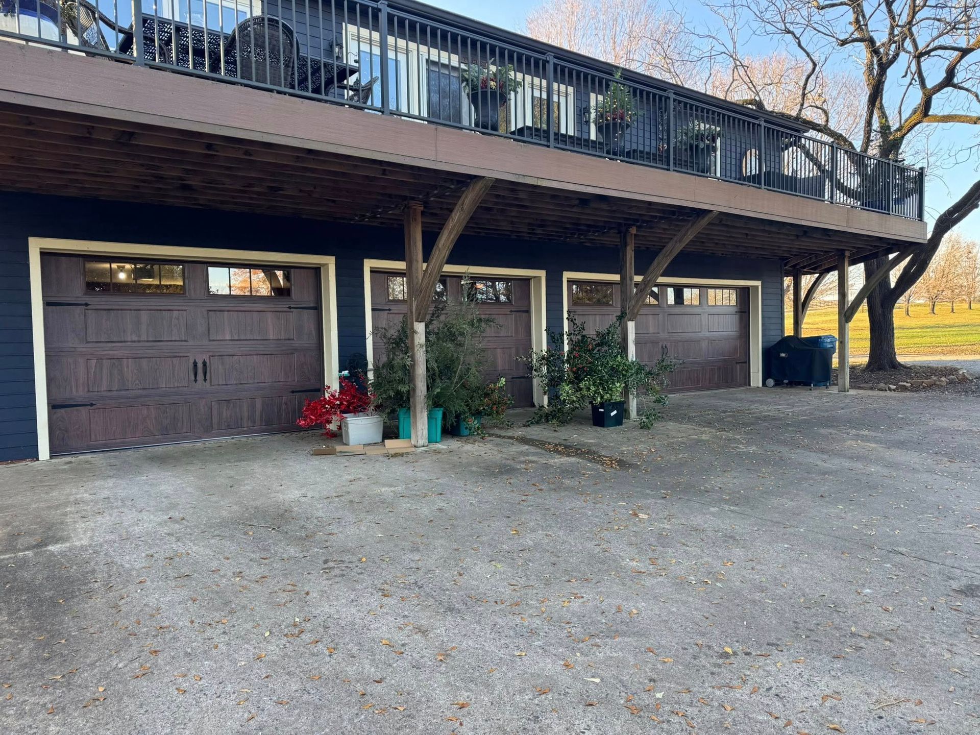 Carport beneath a raised deck with a garage door, gravel driveway, and potted plants.