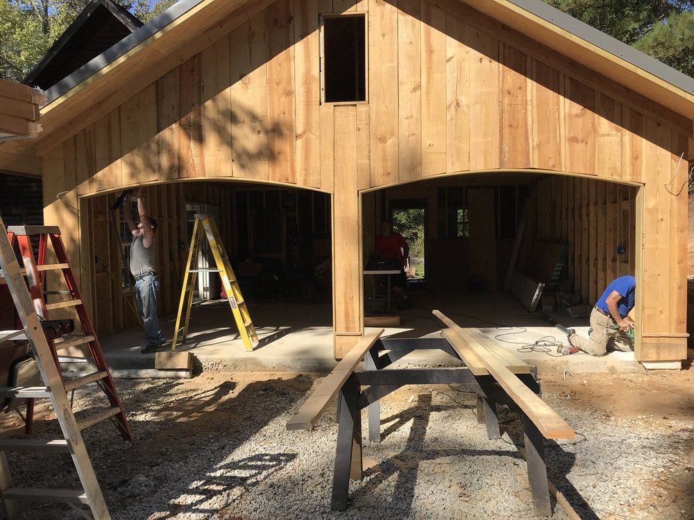 Wood-framed garage under construction with workers, ladders, and lumber in the foreground