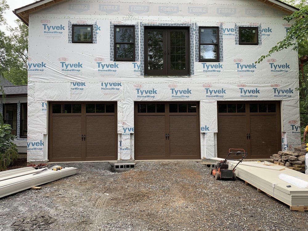 Partially built two-story house wrapped in Tyvek with garage doors and gravel driveway