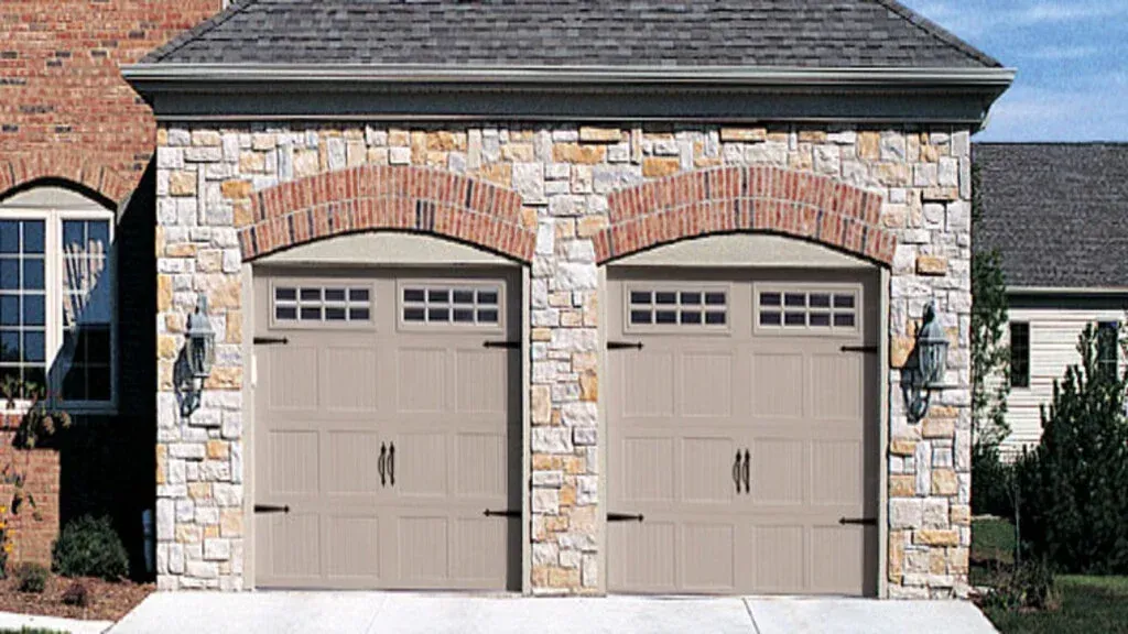 Stone-faced double garage with two beige doors and snow-covered ground in front