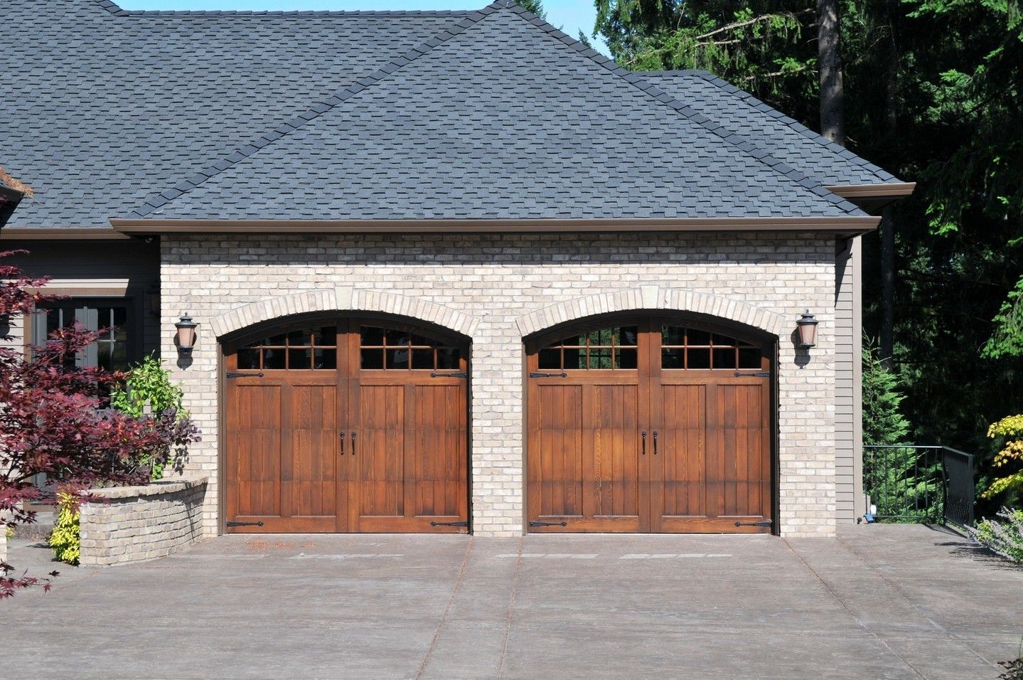 Stone garage with two wooden doors and a gray shingled roof, fronted by a paved driveway.