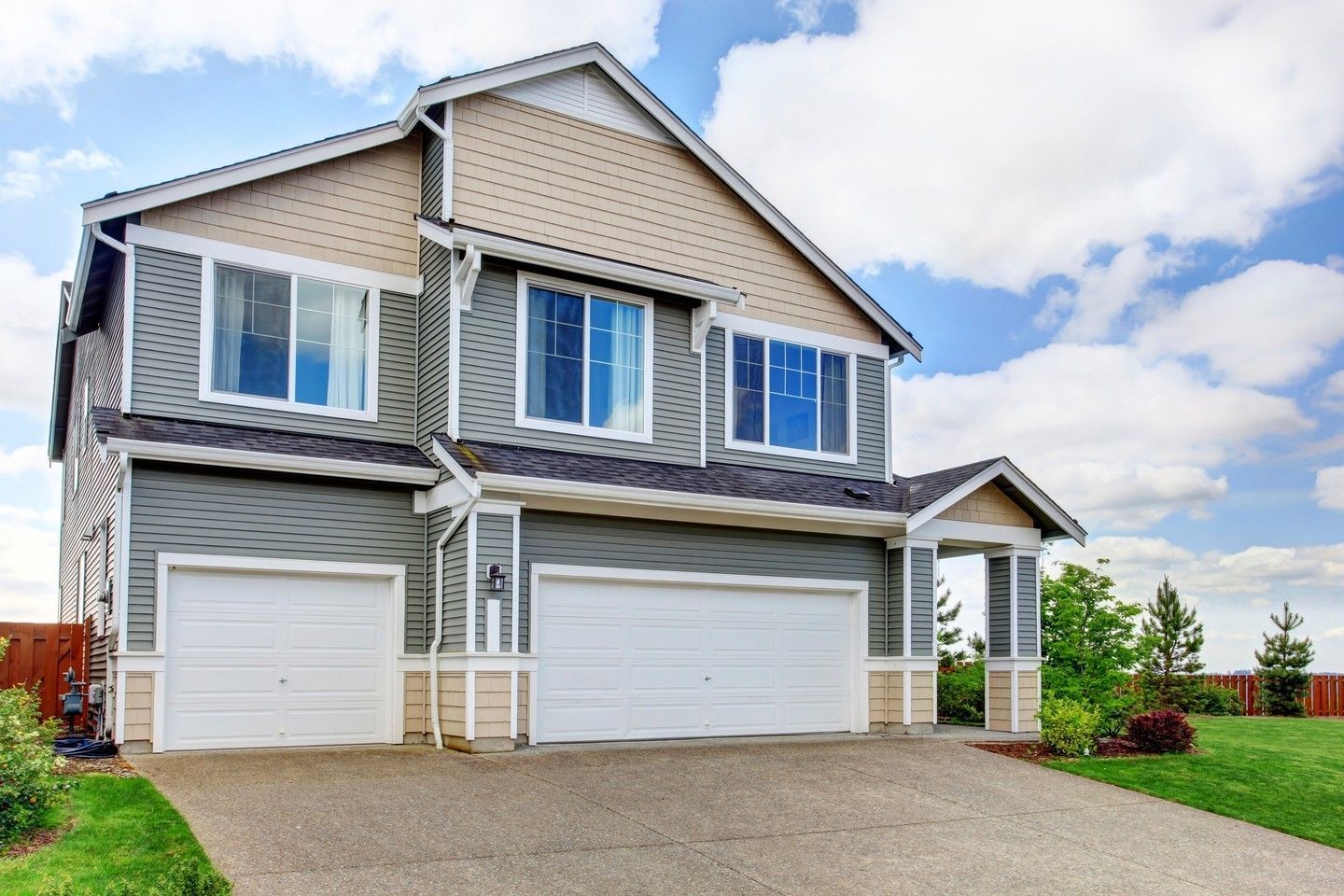 Two-story gray house with white trim, double garage, and a gravel driveway under a partly cloudy sky