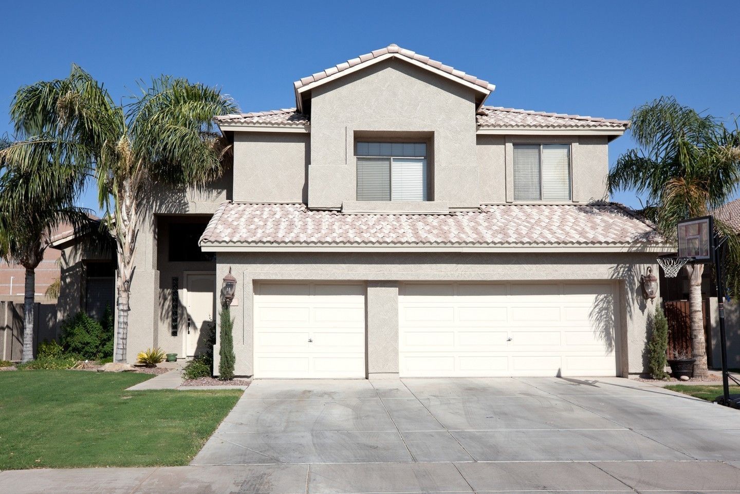 Two-story beige suburban house with a three-car garage and palm trees in front