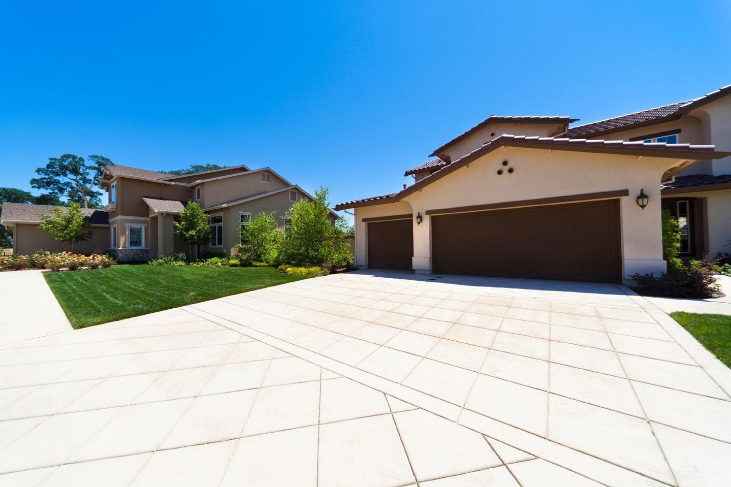 Sunny suburban driveway with two parked garages, green lawn, and blue sky