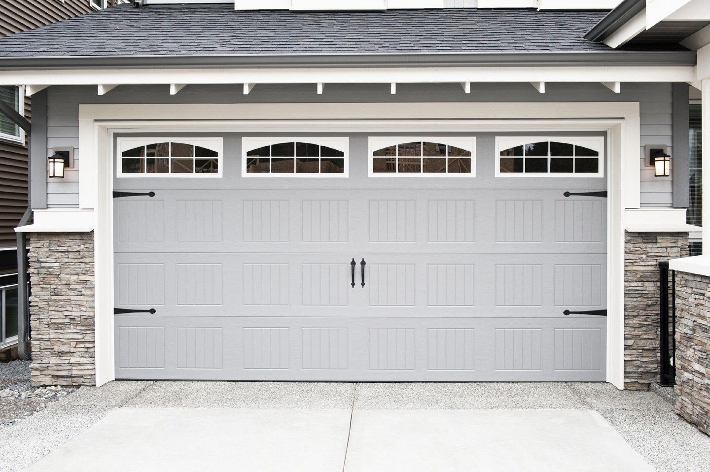 White double garage door with four arched windows on a gray house exterior
