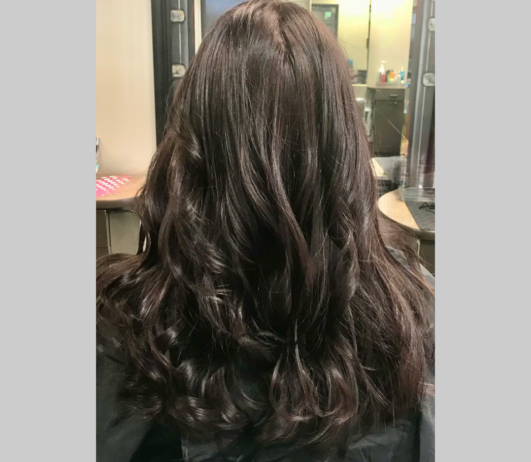 Smooth shiny dark brown hair with soft curls. This is the after picture of a woman's hair.