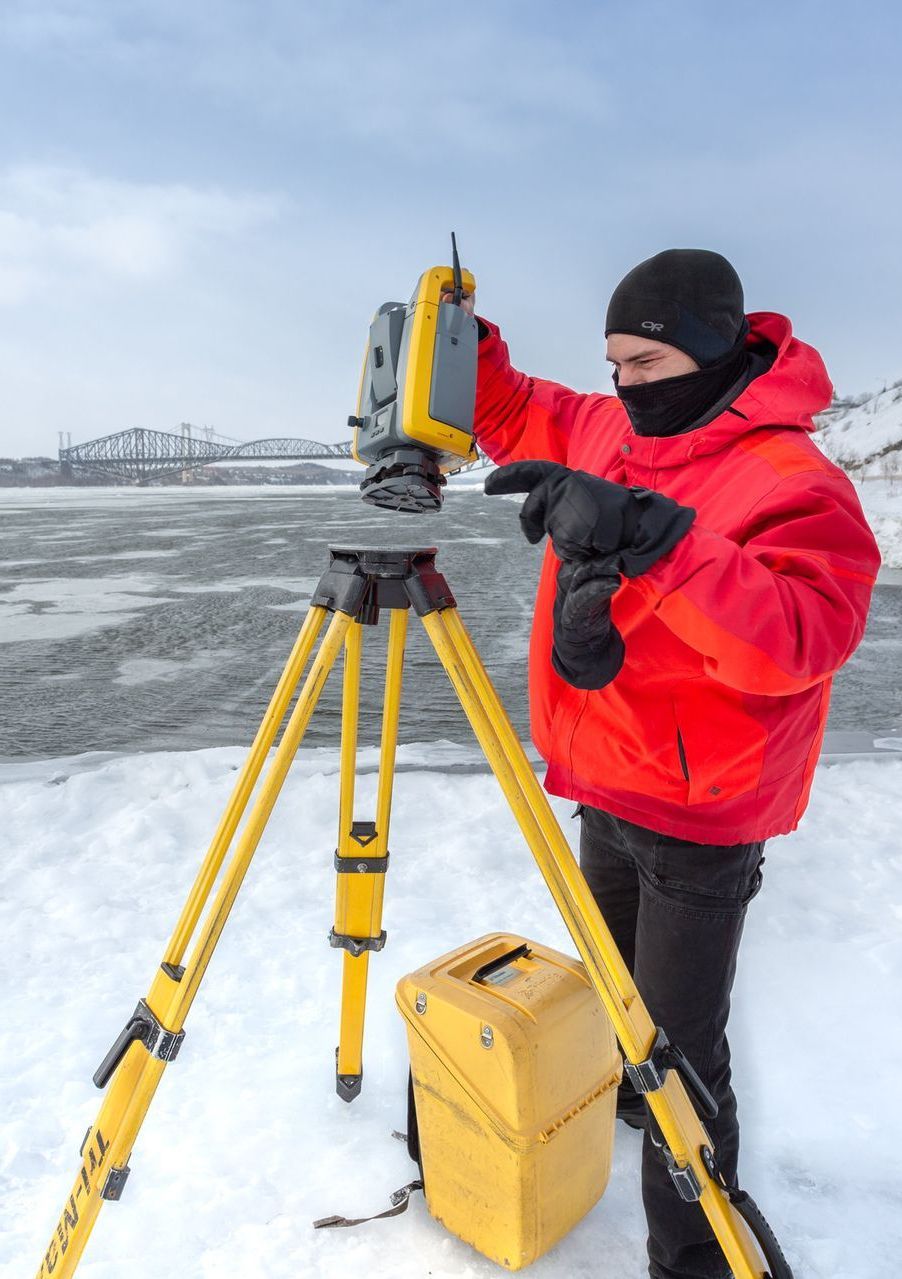 Un homme vêtu d'une veste rouge se tient dans la neige en utilisant un appareil sur un trépied.