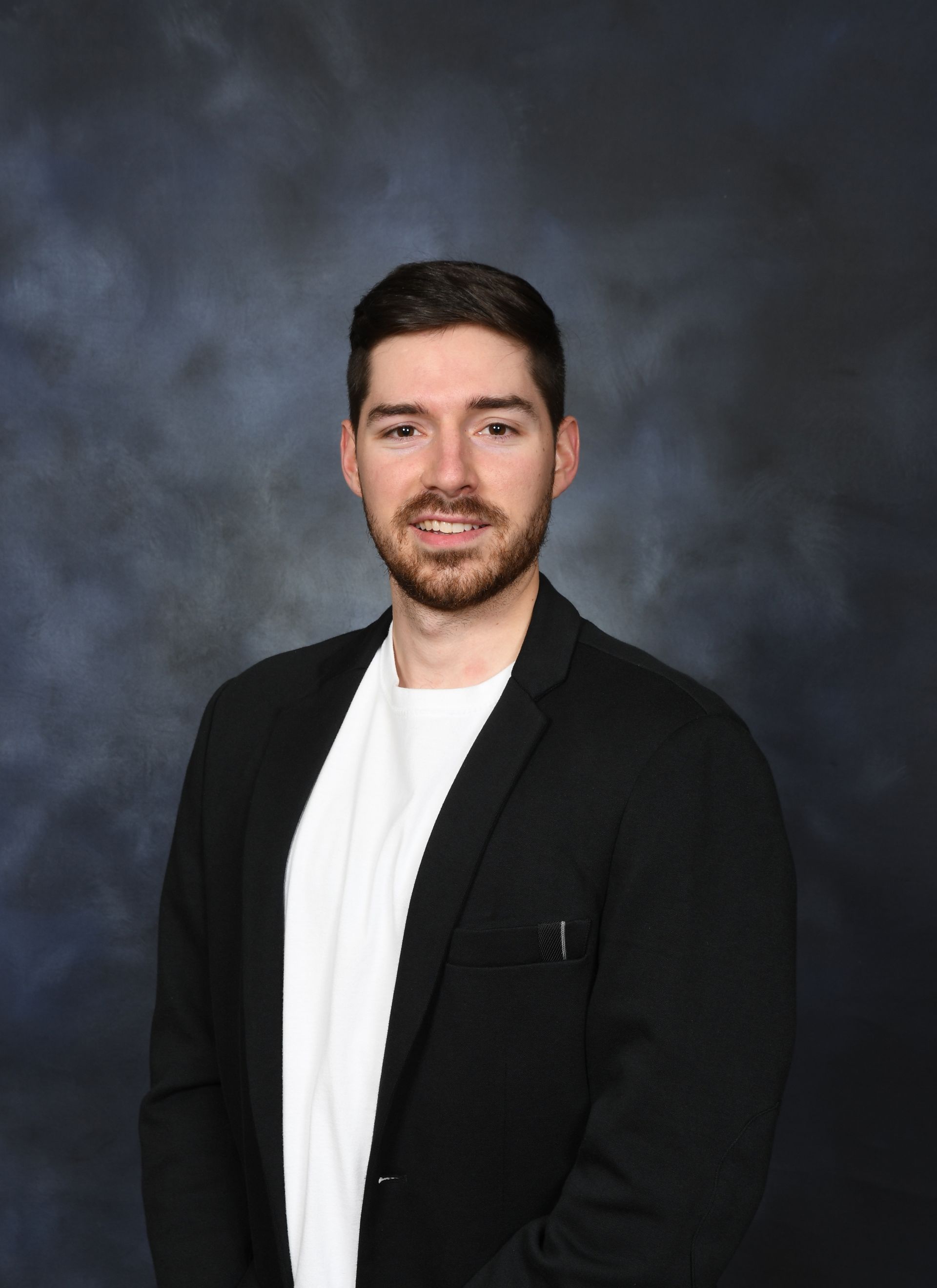 Un homme barbu porte une veste noire et une chemise blanche.