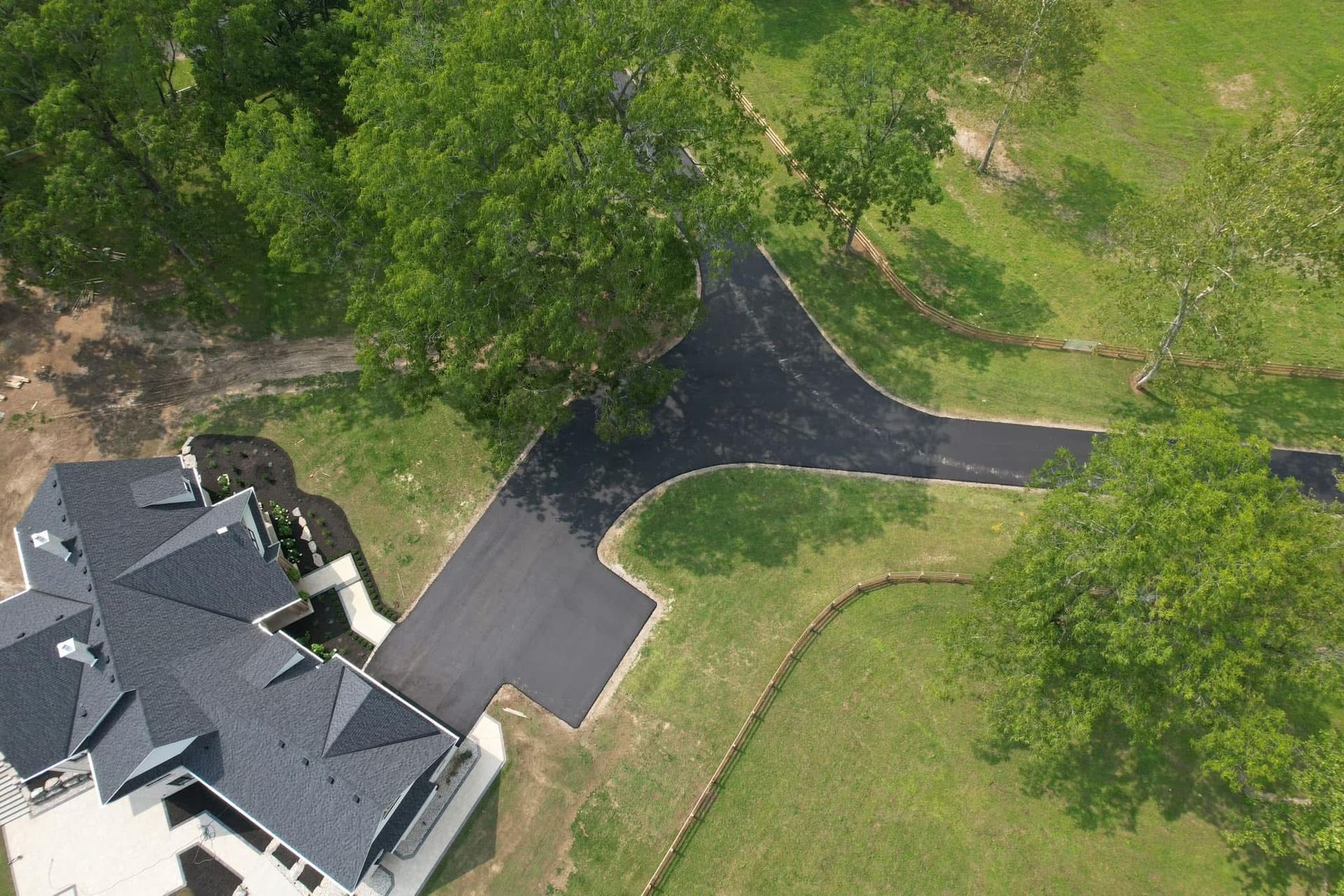 An aerial view of a dark asphalt driveway branching into two paths leading toward a house with a gray roof.