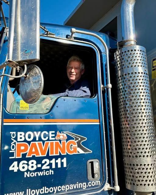 A smiling person sitting in the driver’s seat of a blue Lloyd Boyce Paving truck in Norwich.