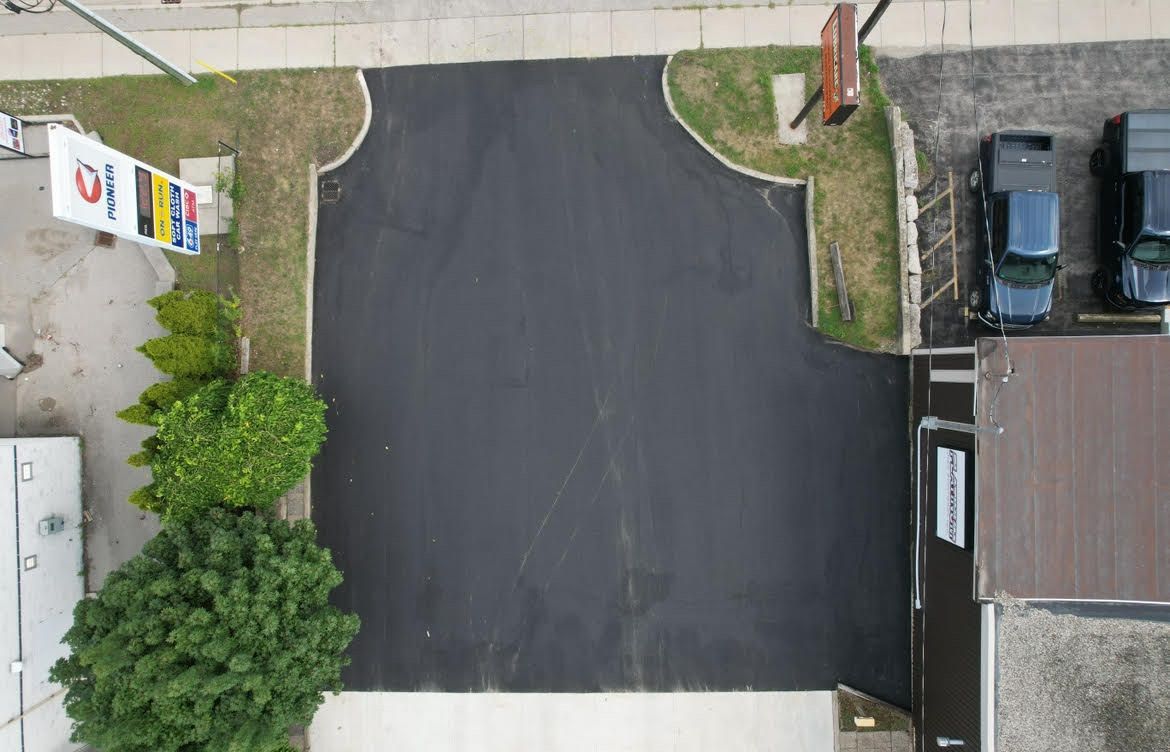 An aerial view of a freshly paved asphalt parking lot adjacent to a building and green space.