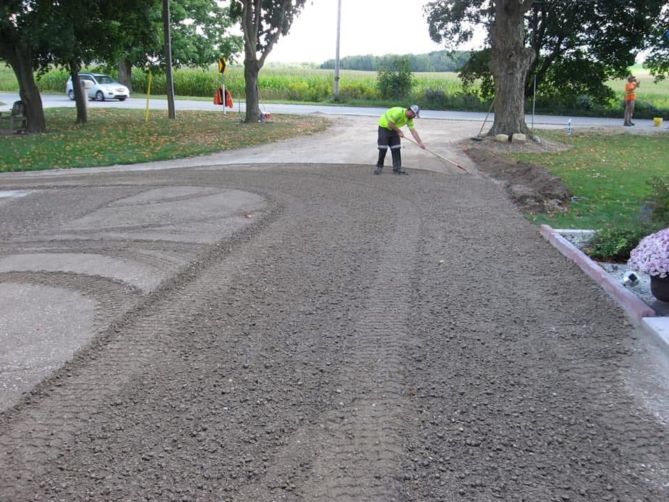 A worker in a high-visibility yellow shirt uses a tool to smooth gravel on a residential driveway.
