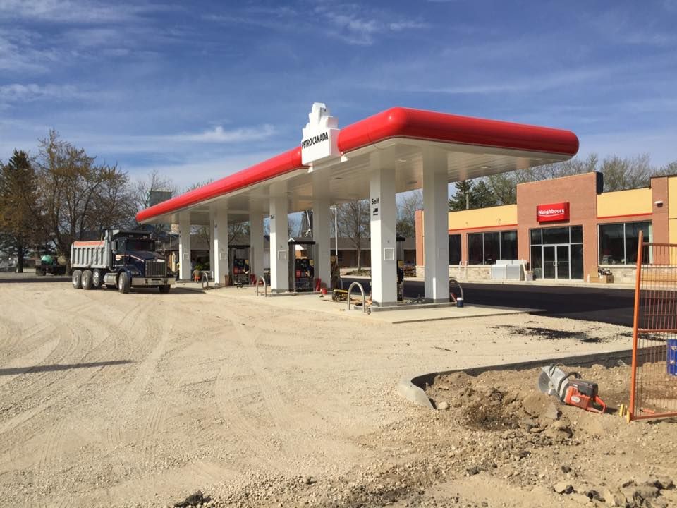 A dump truck parked under the red and white canopy of a gas station under construction on a sunny day.