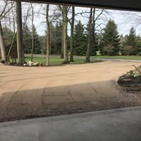 A view from a garage looking out at a large gravel driveway surrounded by trees and lawn.