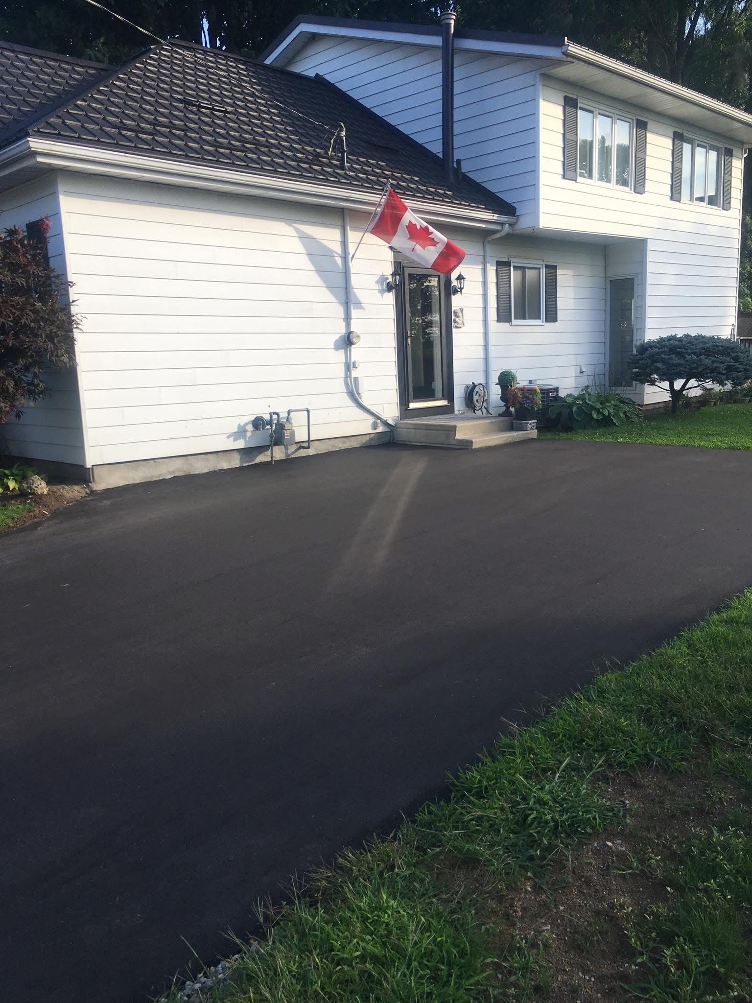 A two-story white house with a dark roof and driveway, featuring a small Canadian flag by the front entrance.