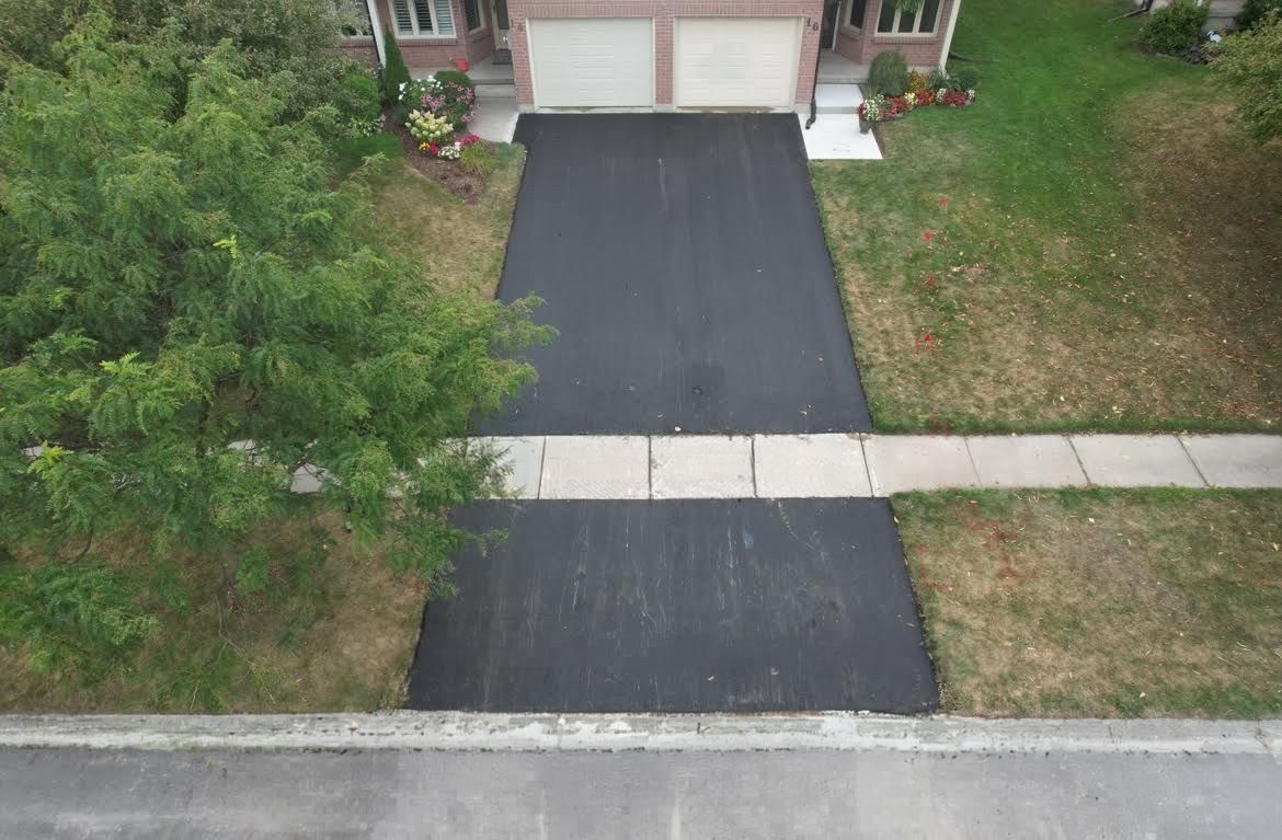 An aerial view of a black asphalt driveway leading from a street, crossing a sidewalk, to a house with two garage doors.