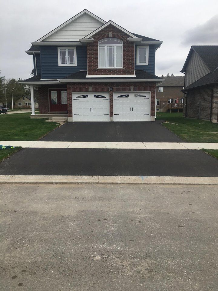 A two-story house with blue siding, brick accents, and a double garage, facing a paved driveway and suburban street.