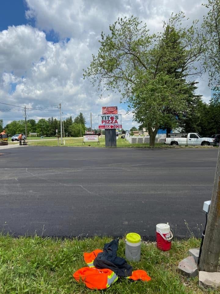 A parking lot with a Tito’s Pizza sign in the background, with high-visibility gear and water coolers in the foreground.