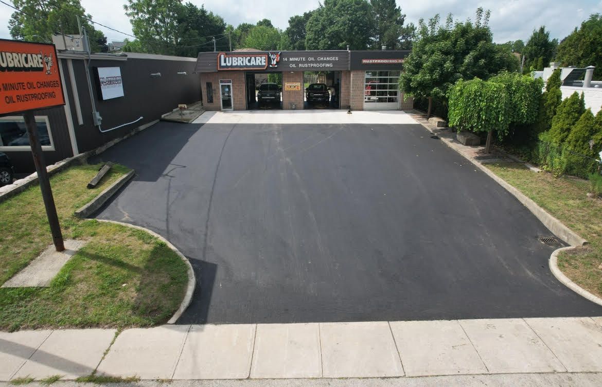 A freshly paved, dark asphalt parking lot in front of a brick commercial building with three service garage bays.
