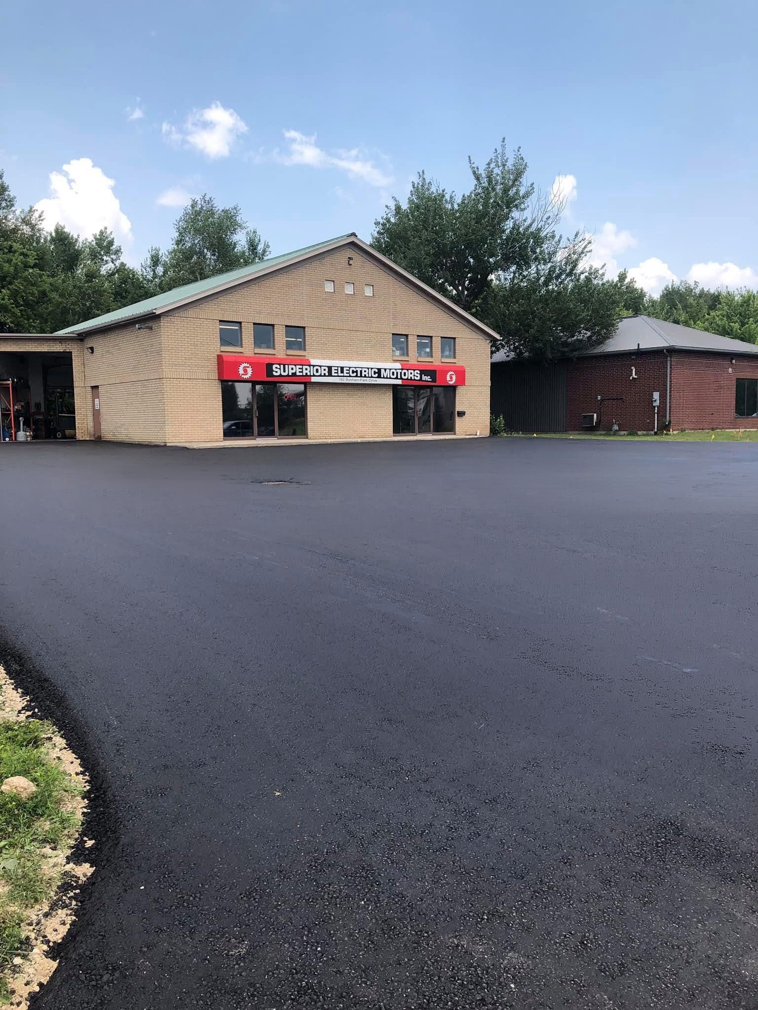 A tan commercial building with a red sign, featuring a newly paved asphalt parking lot under a bright blue sky.