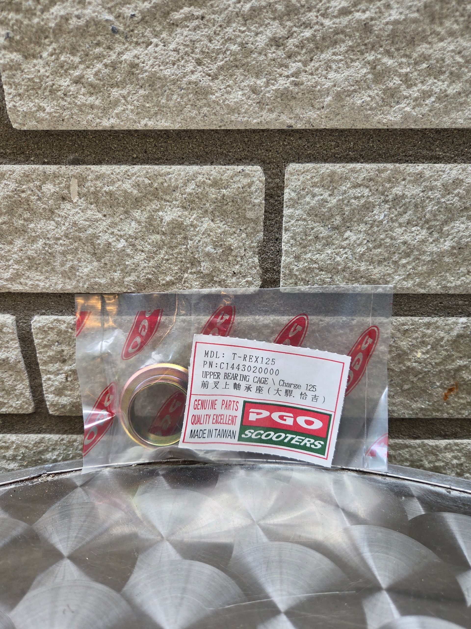 Een klein verpakt artikel met een Japans etiket en een ring liggen op een metalen ondergrond tegen een stenen muur.
