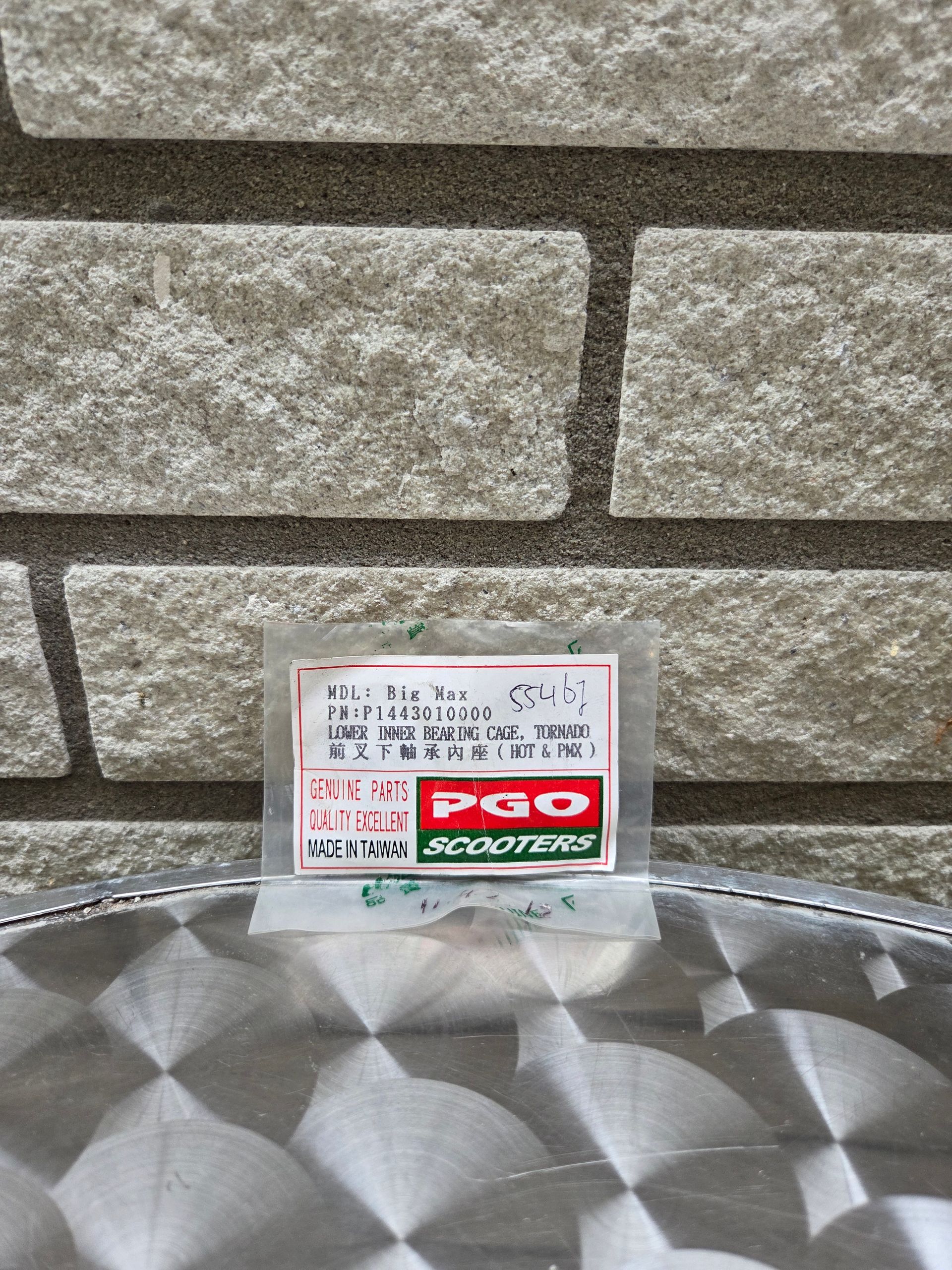 Klein productetiketje, geplaatst op een zilverkleurig, gestructureerd oppervlak tegen een stenen muur.