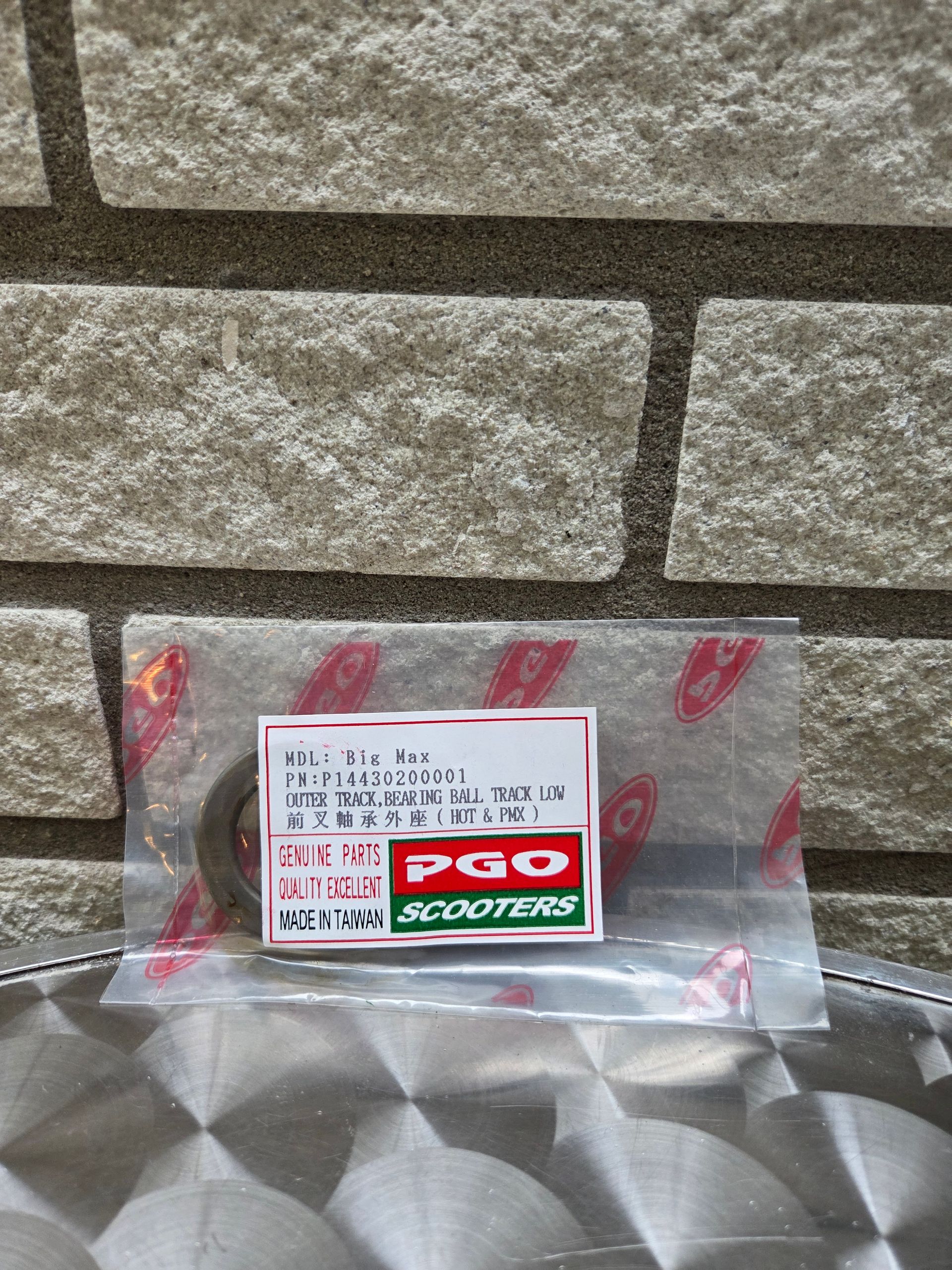 Het doosje van een kleine PGO-scooter in een doorzichtige plastic zak, op een metalen ondergrond tegen een stenen muur.