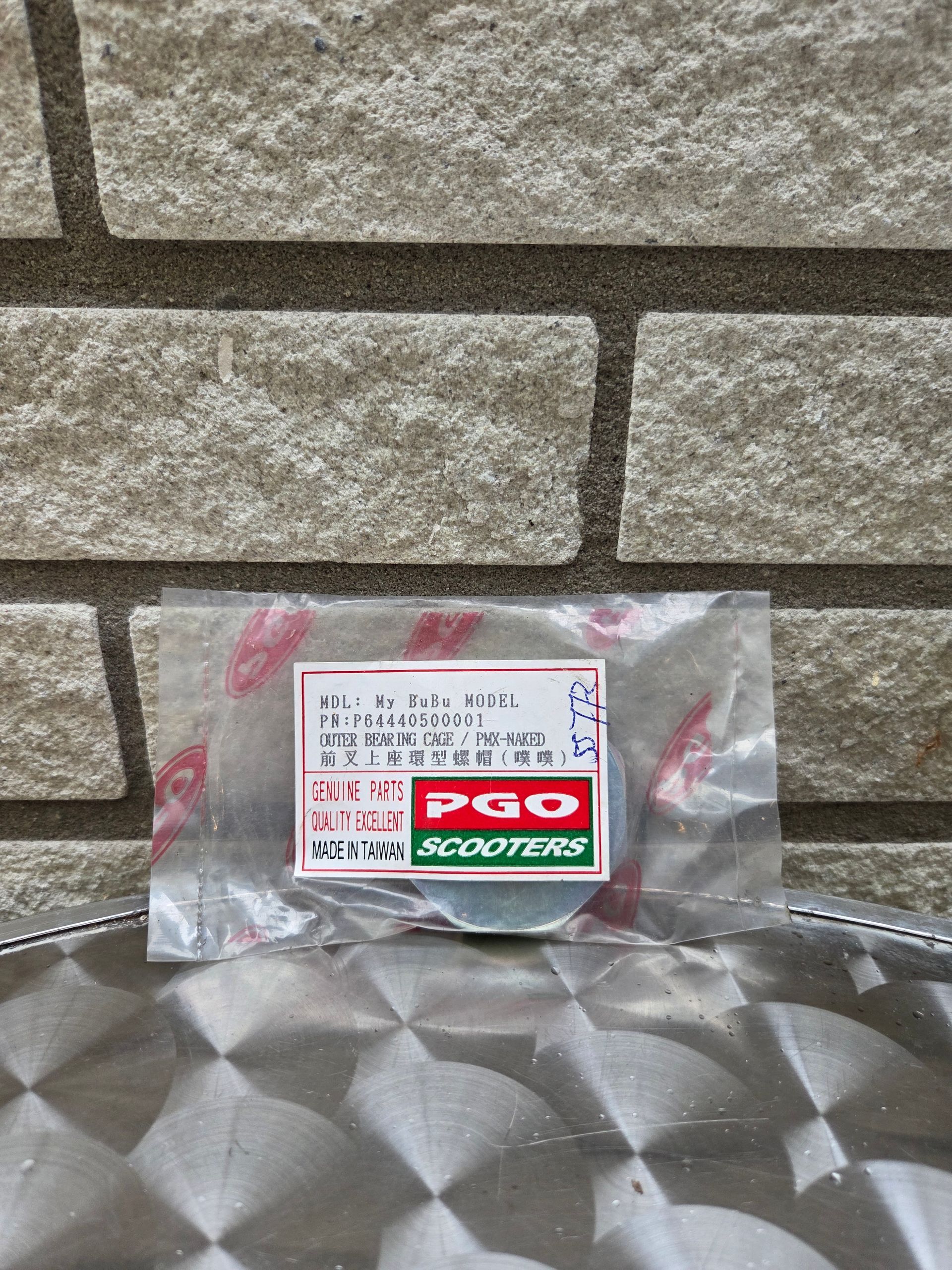 Klein, doorzichtig plastic zakje met een wit etiket en een rood-groen logo op een metalen ondergrond tegen een stenen muur.