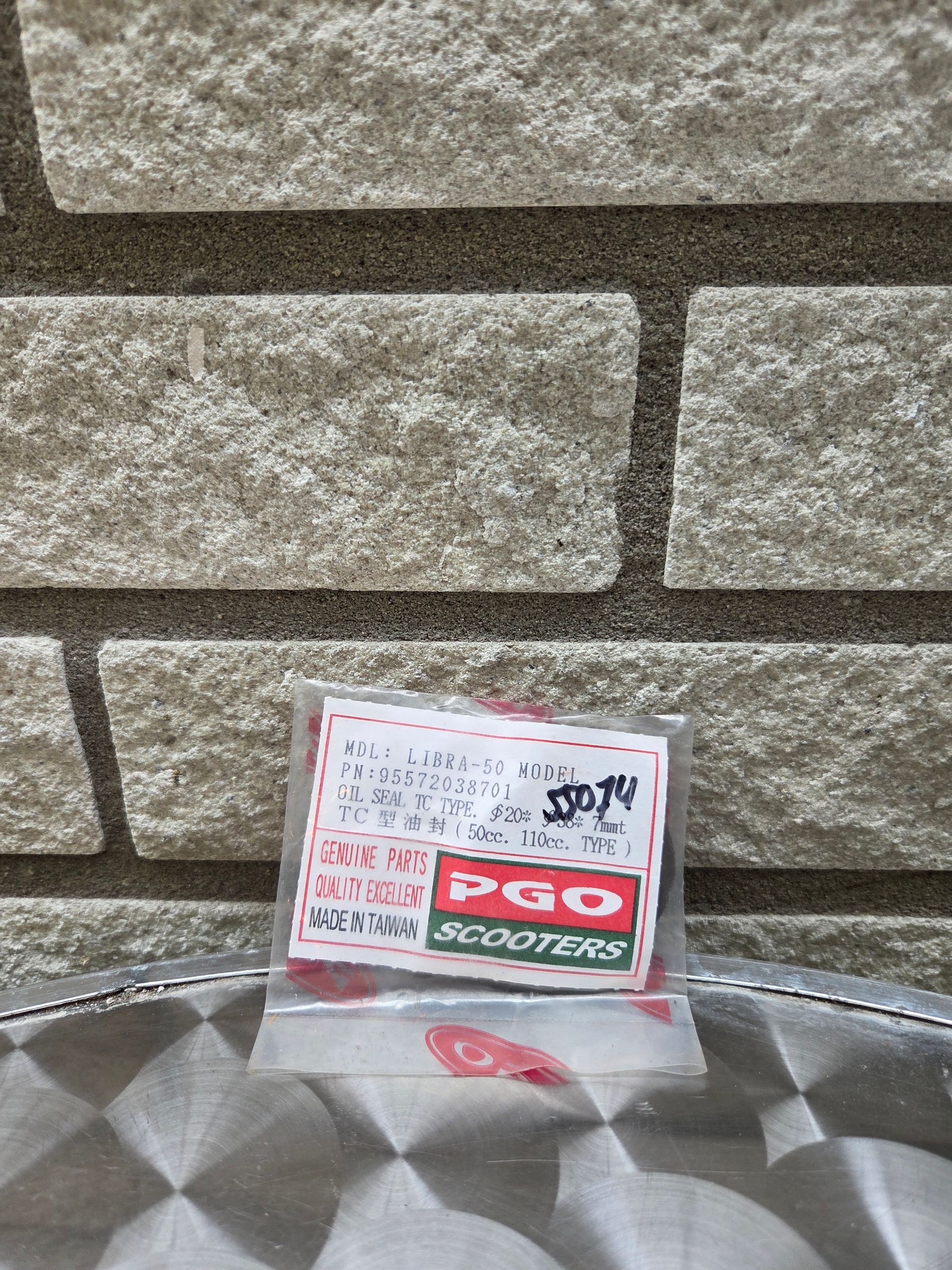 Kleine PGO-sticker die tegen een stenen muur op een metalen ondergrond leunt.