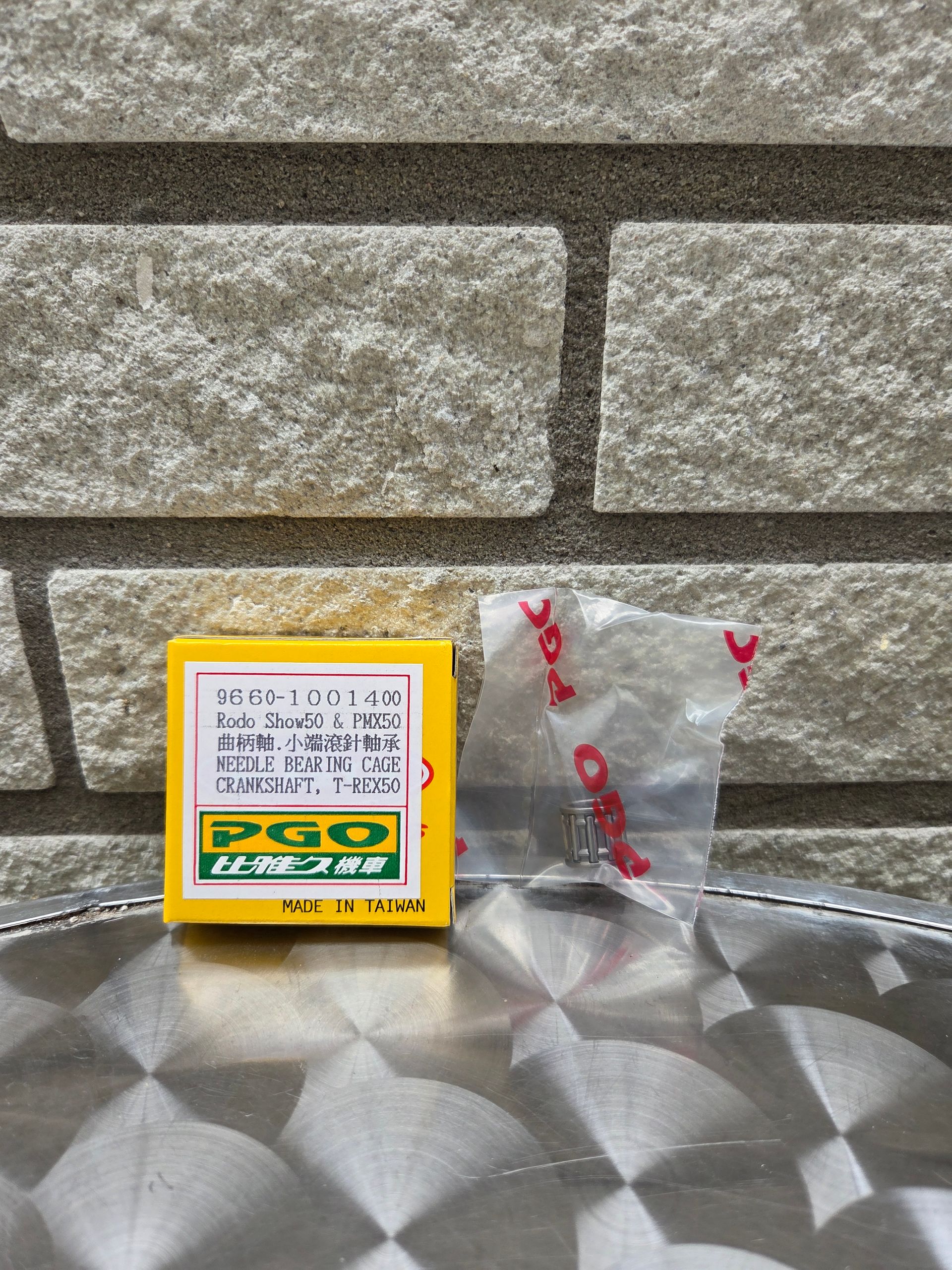 Een klein geel doosje en een doorzichtig plastic zakje op een metalen tafel tegen een stenen muur.