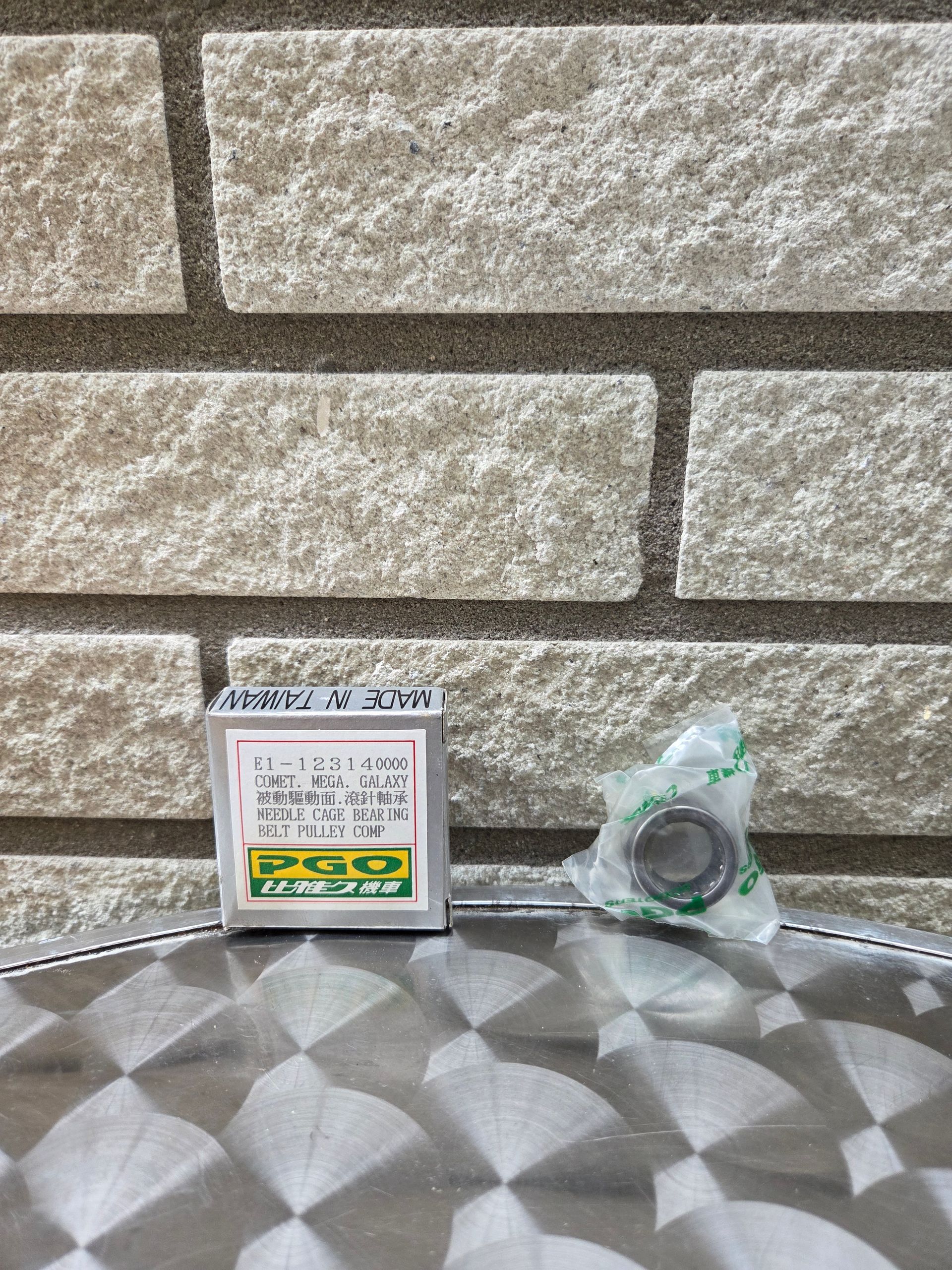 Een klein doosje en een doorzichtige plastic zak op een ondergrond met patroon, tegen een stenen muur.