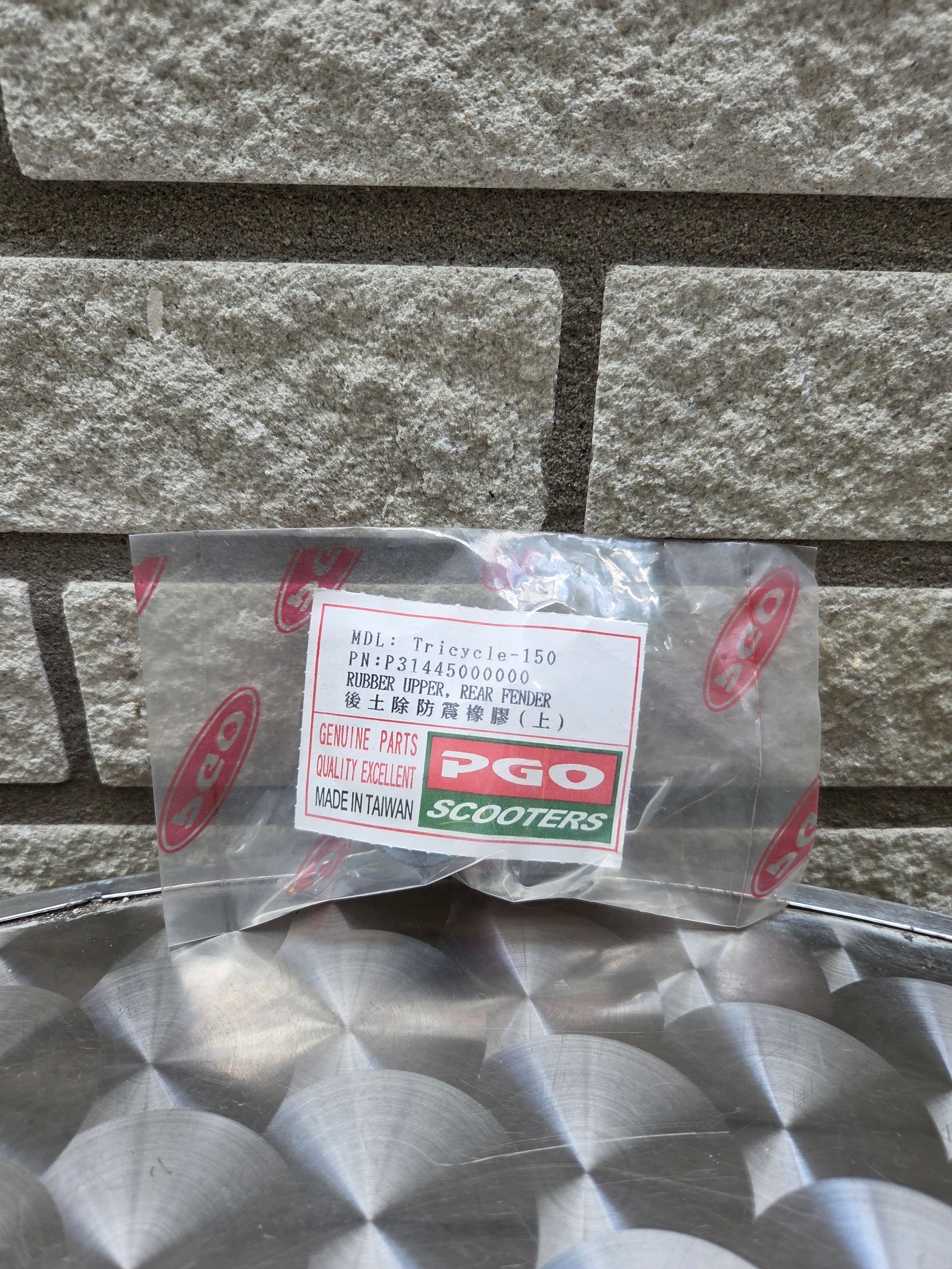 Een doorzichtige plastic zak met een rood-groen etiket staat tegen een bakstenen muur op een metalen ondergrond.