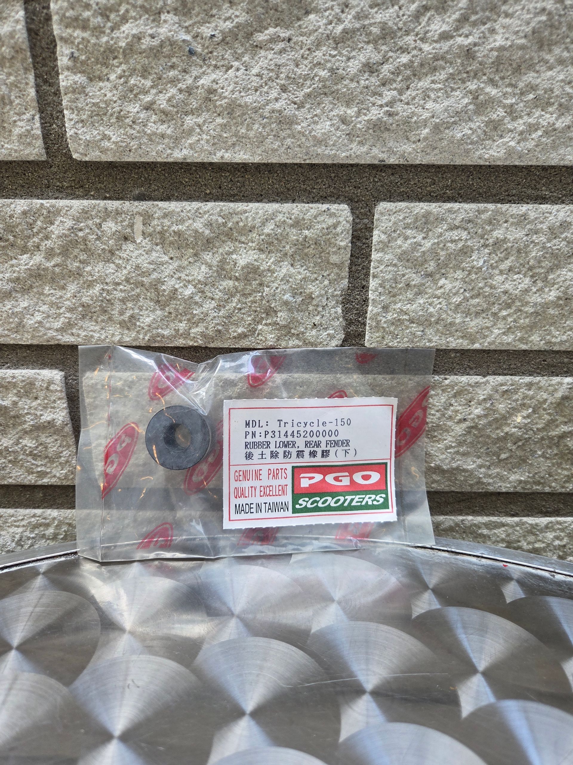 Een doorzichtige plastic zak met een klein rood-wit etiket op een muur van natuursteen met structuur, boven een metalen oppervlak.