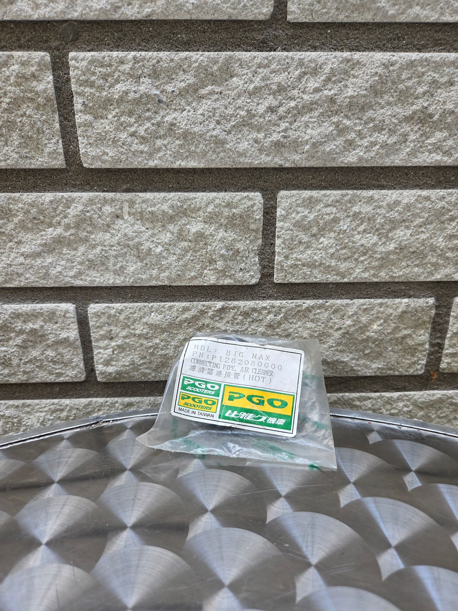 Een klein groen-wit pakje ligt op een zilverkleurig tafelblad met structuur, voor een stenen muur.