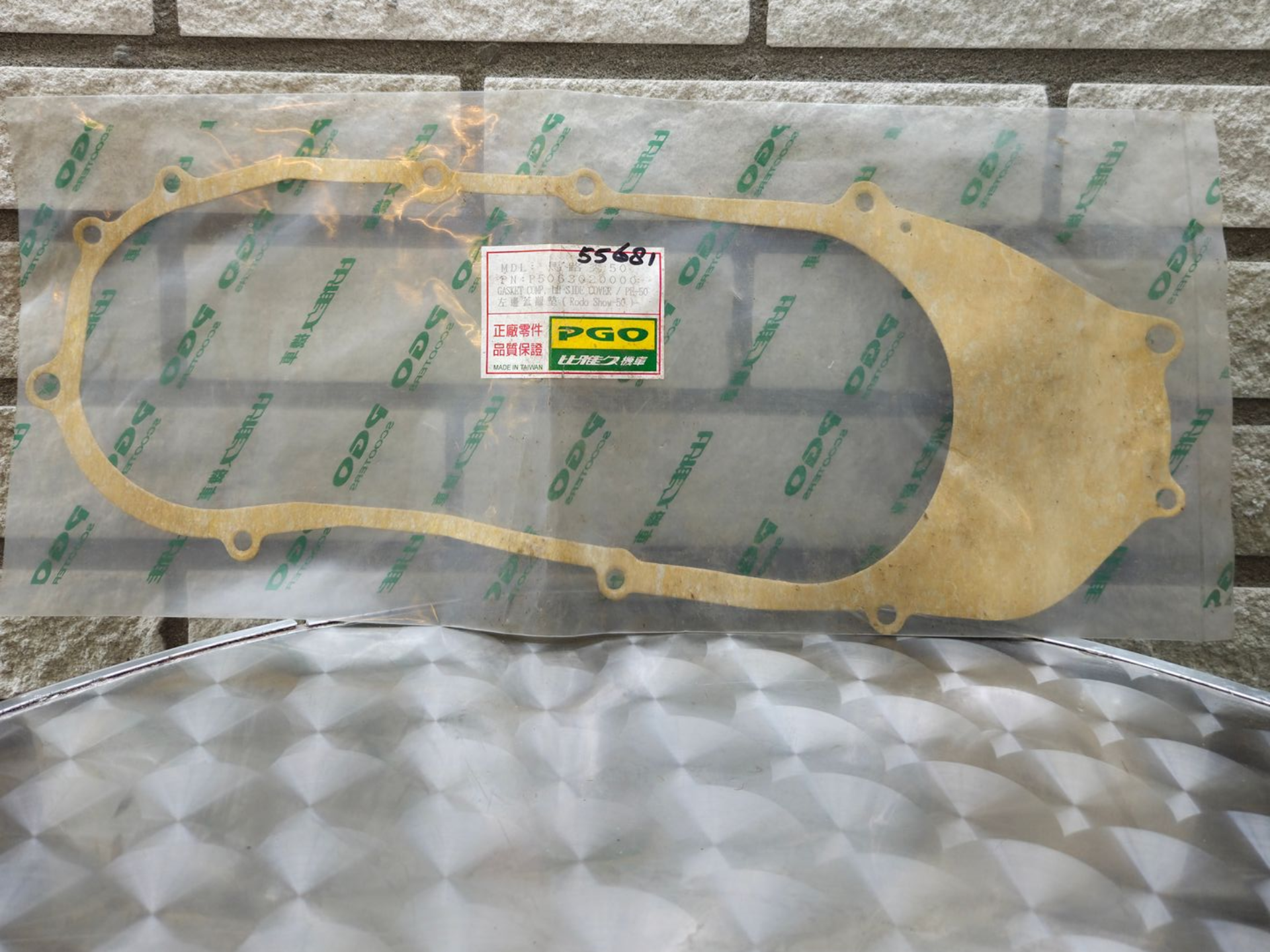 Pakkingset in een transparante plastic verpakking op een zilverkleurige ondergrond met patroon, met gele en grijze pakkingstukken.