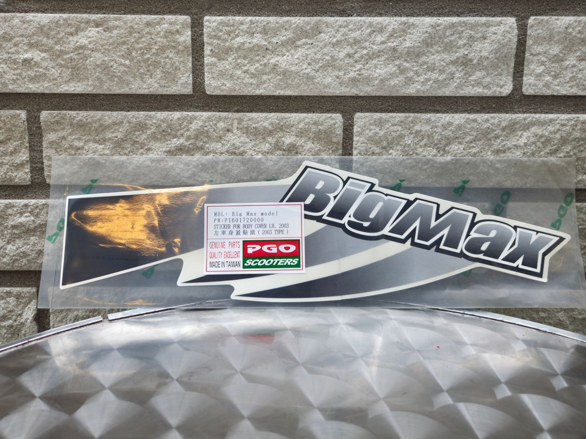 BRUMAX productlabel op een transparante plastic verpakking met een bakstenen muur op de achtergrond en een reflecterend oppervlak.