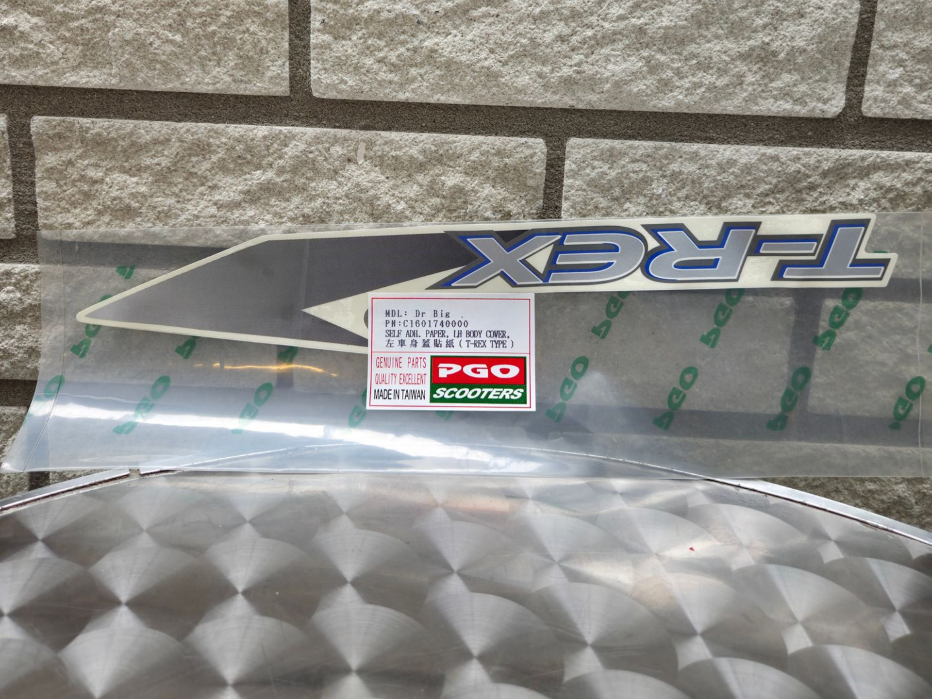 Tamiya TRF X carrosserie met stickers, grijs en zilver, tentoongesteld tegen een bakstenen muur.