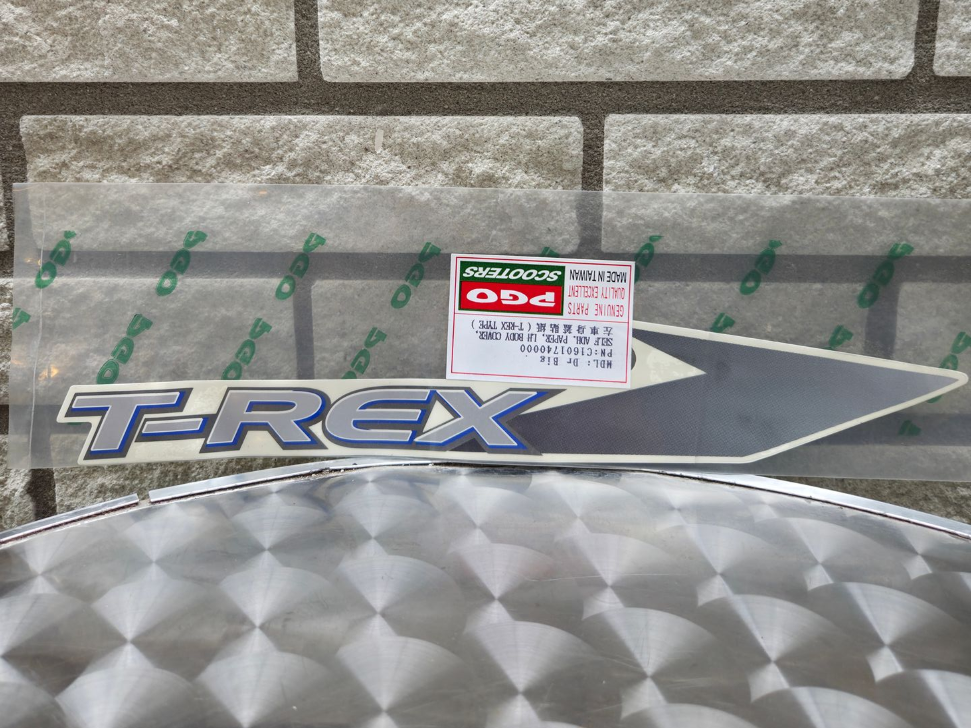 Tamiya TRF X carrosserie met stickers, grijs en zilver, tentoongesteld tegen een bakstenen muur.
