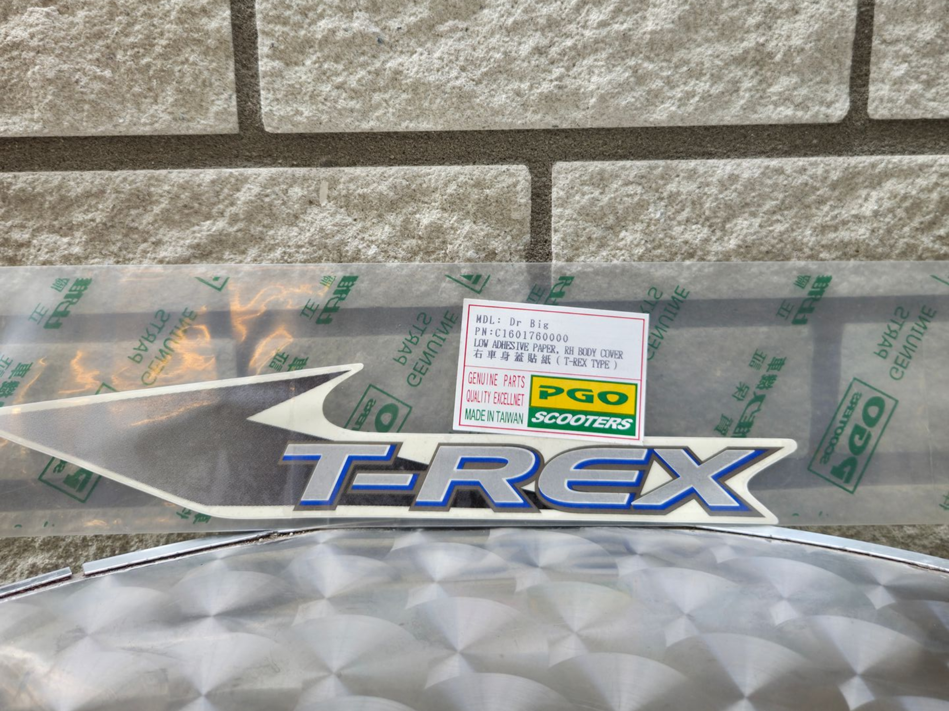 T-REX logo sticker met een transparante beschermfolie en een kleine prijssticker op een stenen muurachtergrond.
