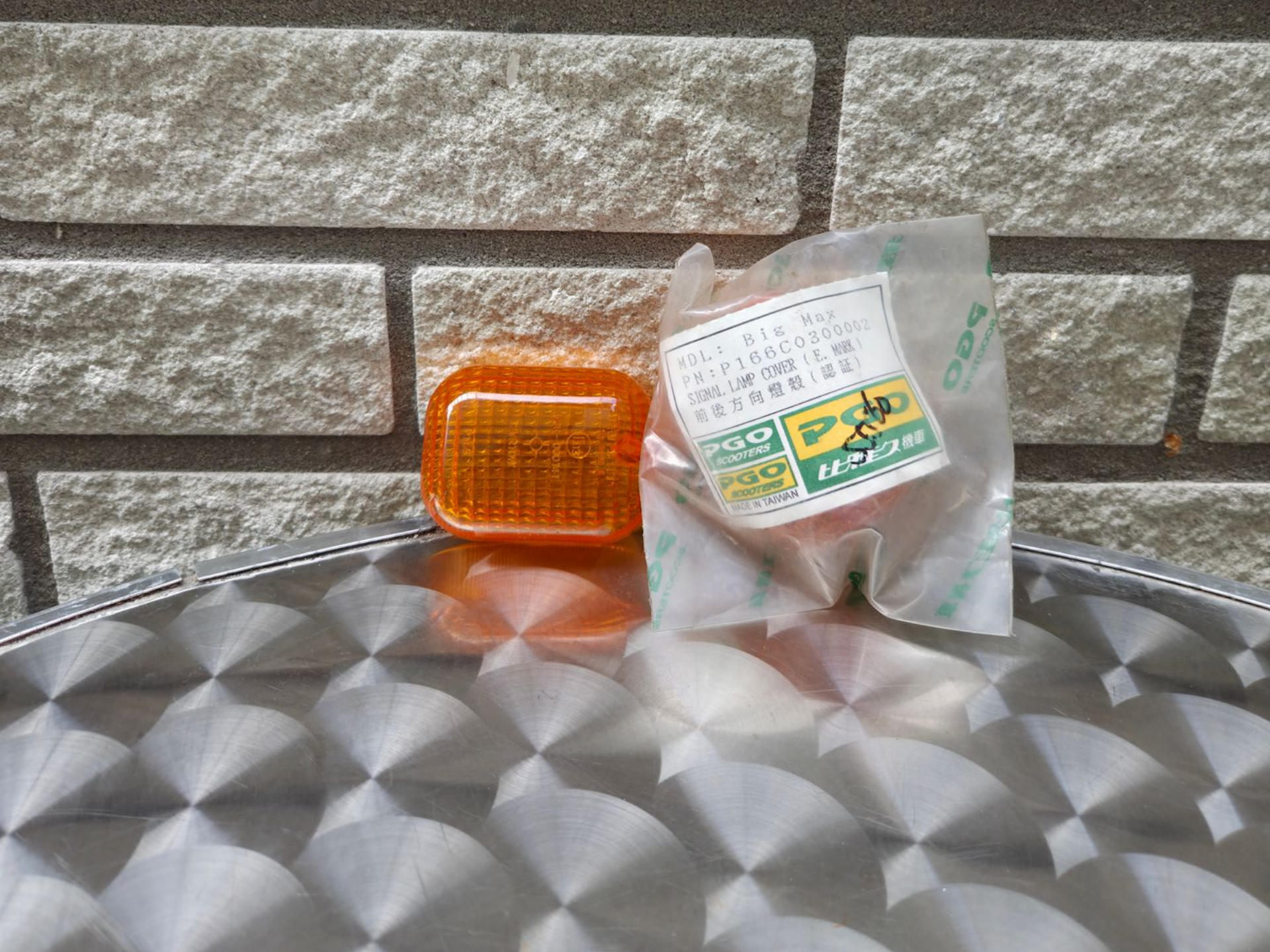 Een oranje reflector en een doorzichtige plastic zak met etiketten op een metalen tafelblad tegen een bakstenen muur.