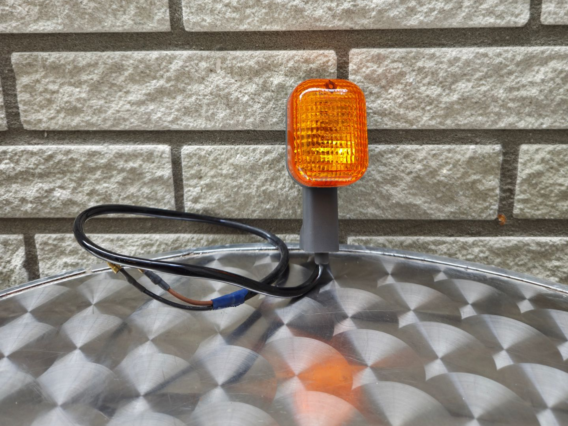 Amberkleurig zwaailicht met zwarte kabel op een metalen oppervlak tegen een bakstenen muur.