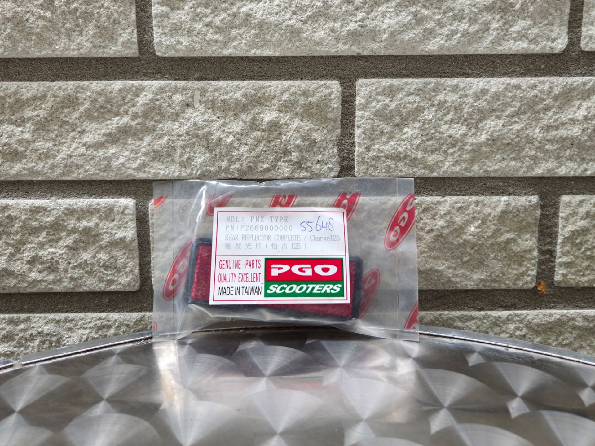 Een klein, doorzichtig plastic zakje met een rood-wit etiket ligt op een metalen ondergrond tegen een stenen muur.