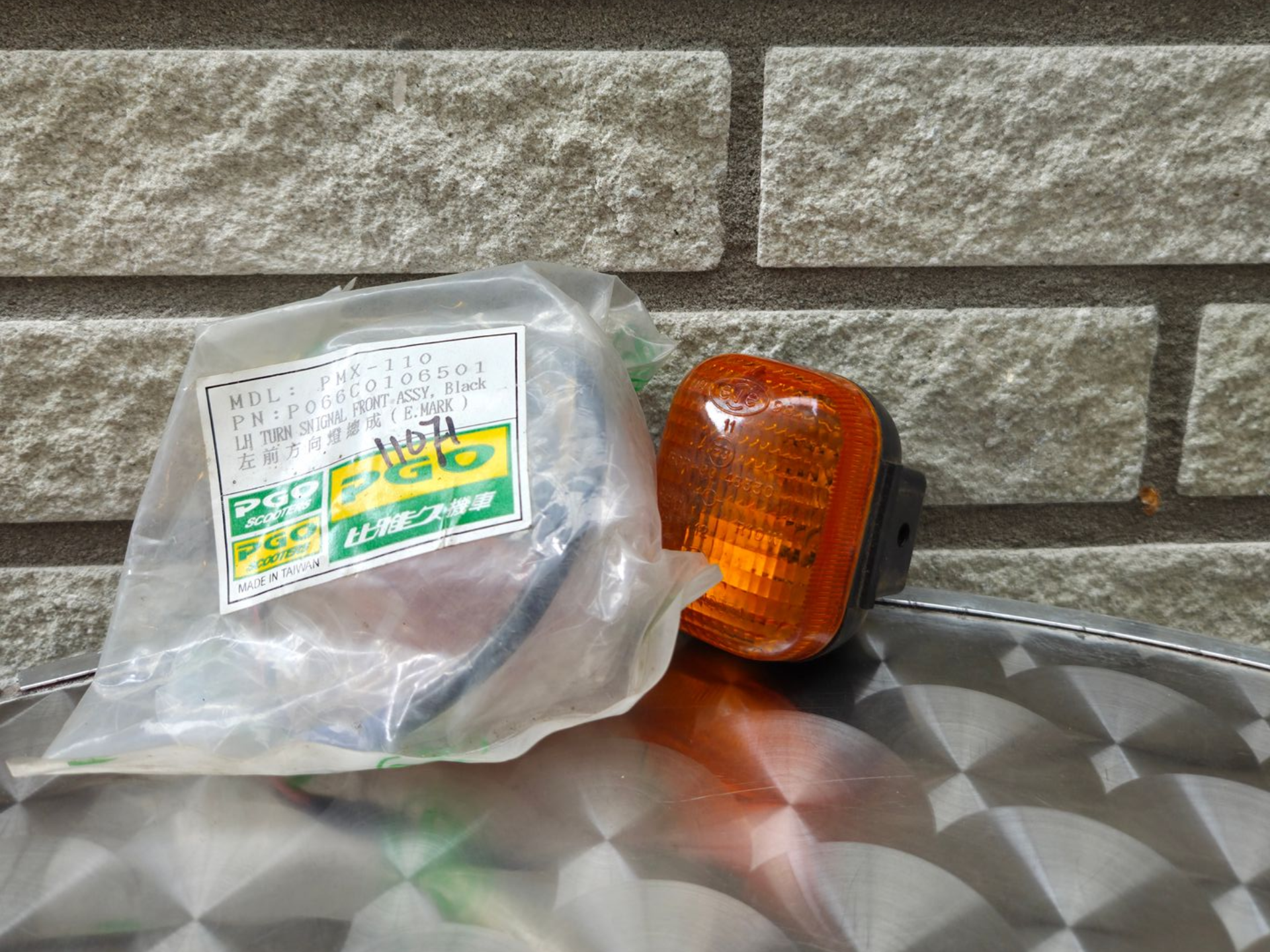 Een in plastic verpakte oranje autokoplampunit op een oppervlak met patroon tegen een stenen muur.